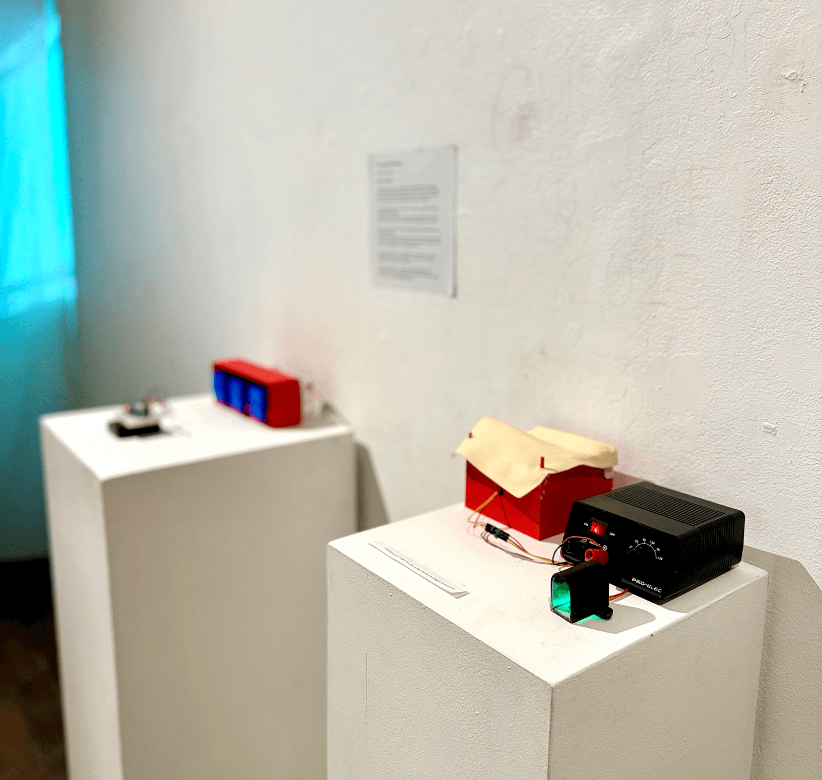 The Huggables installation on white gallery podiums: body pillows and small electronic devices