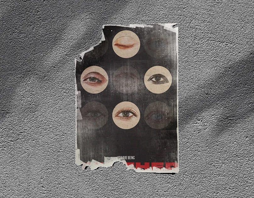 A torn collage poster of cut-out human eyes on a grey textured wall, with the words “You are being” over red lettering