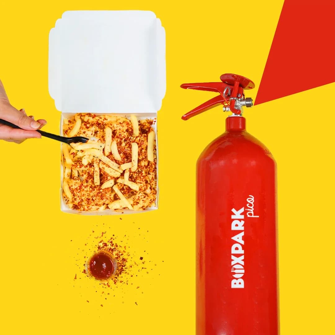 Spicy chili fries in a box beside a red BoxPark-branded fire extinguisher
