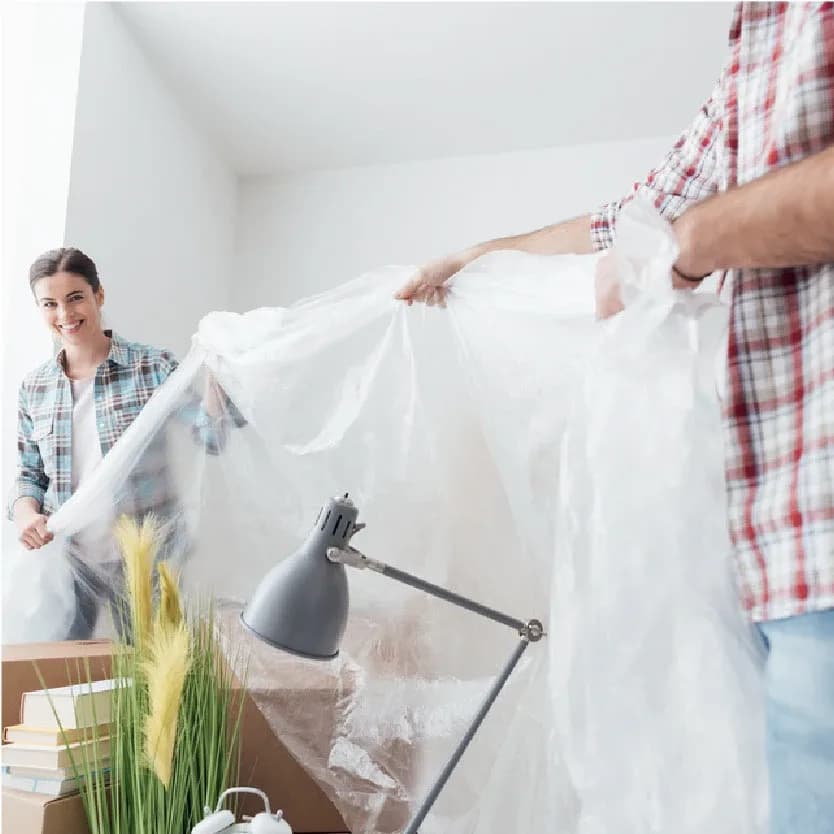 Two people spreading a dust sheet over furniture