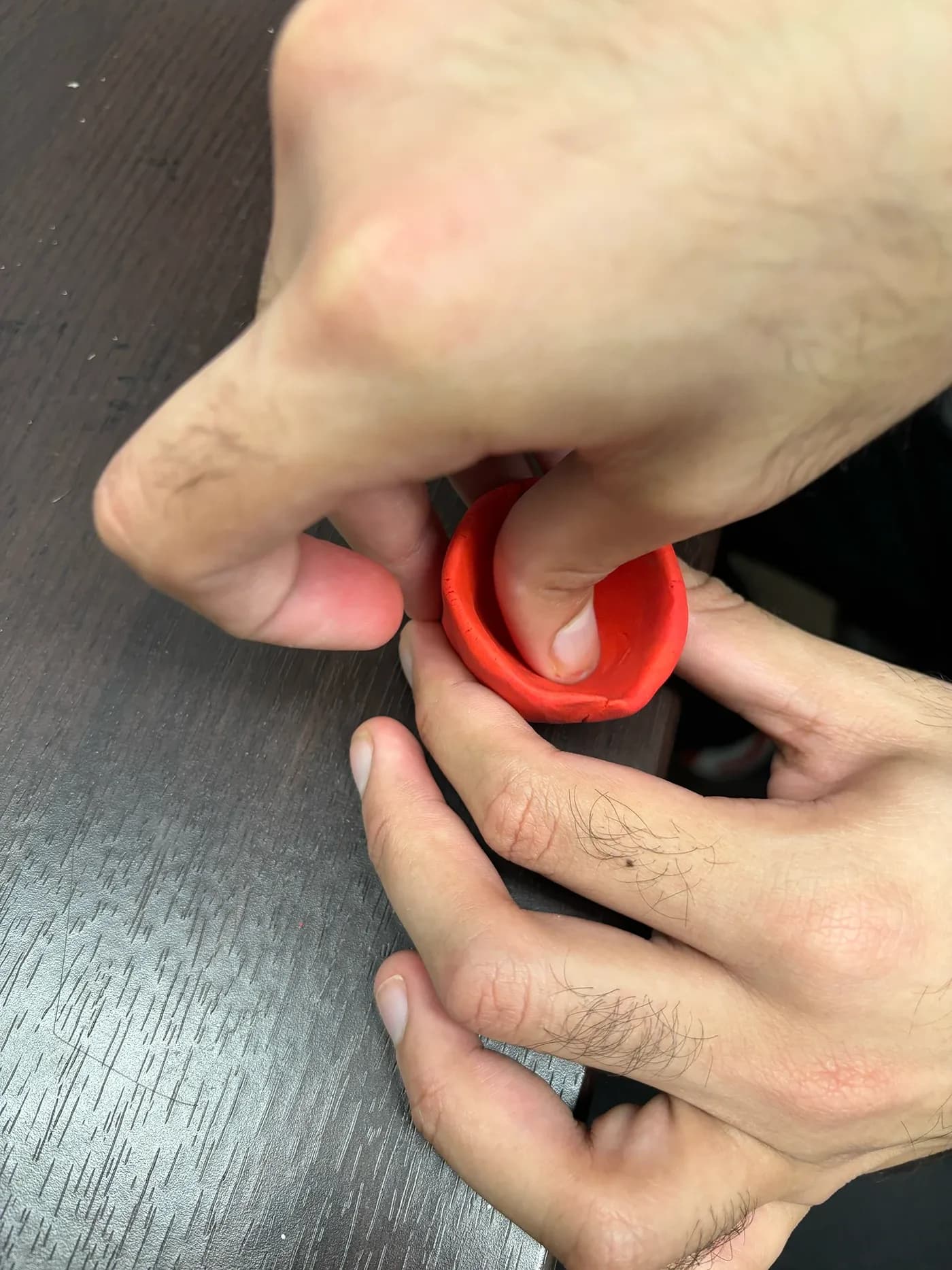 Hands shaping red modeling clay into a bowl