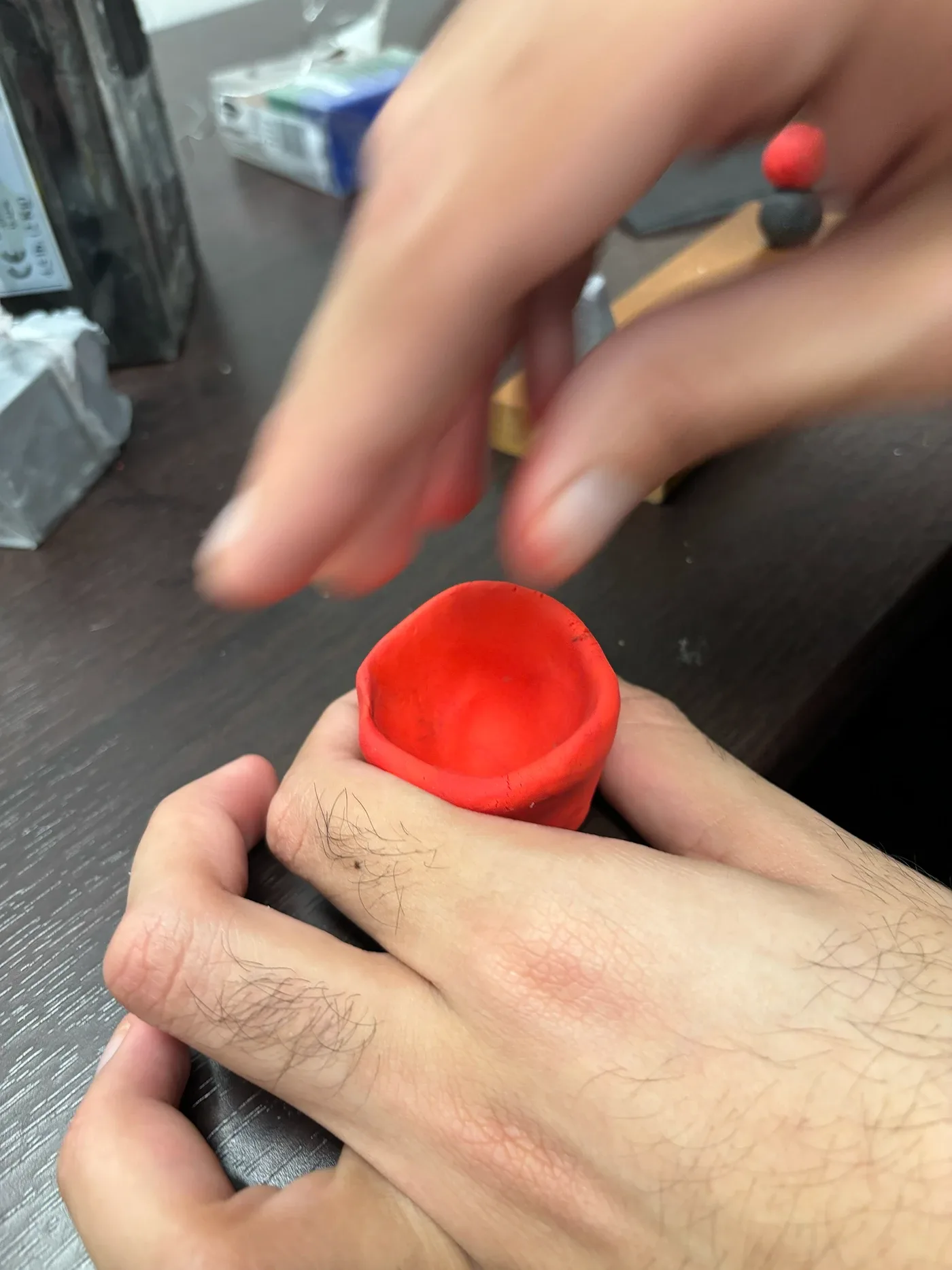 Hands refining the rim of the red clay bowl