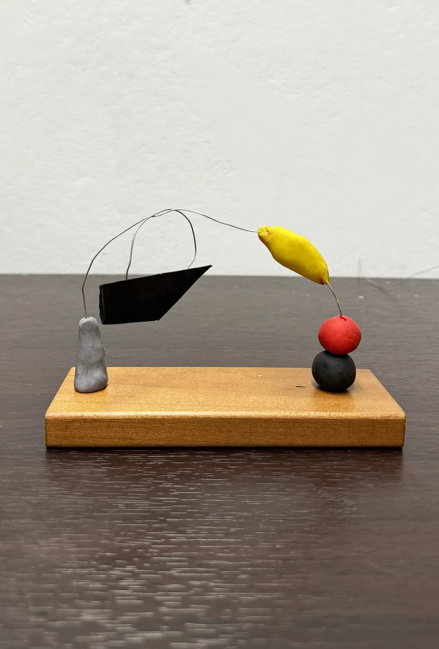 Kinetic sculpture with a black wing, yellow and red forms on a wood base