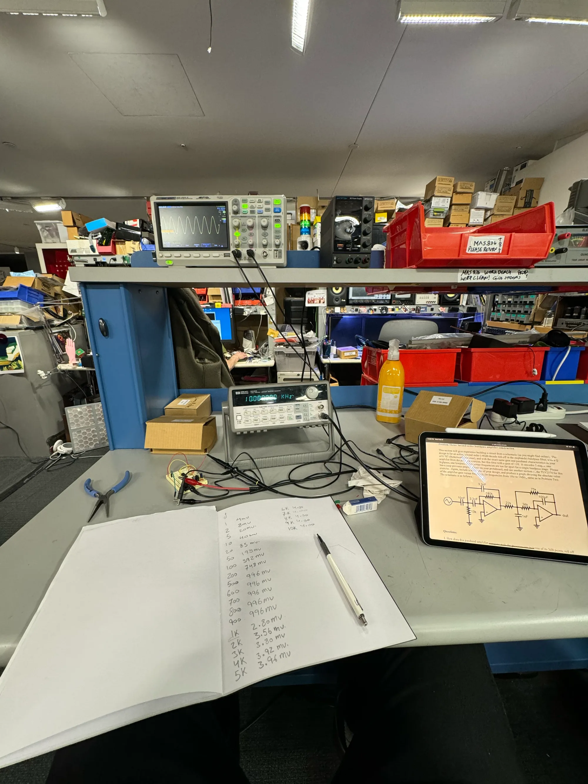 Lab bench with oscilloscope, notebook and circuit schematic on a tablet