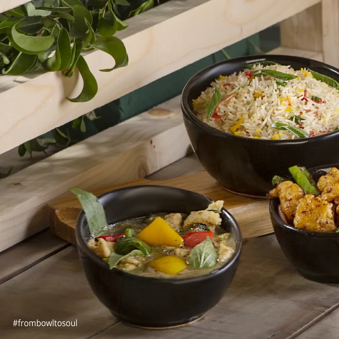 Green curry and fried rice in black bowls on a wooden table