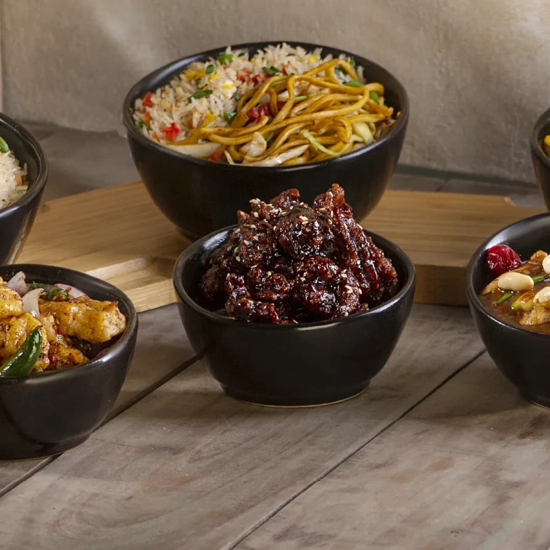 Black bowls of noodles, rice and sesame-glazed beef on wood