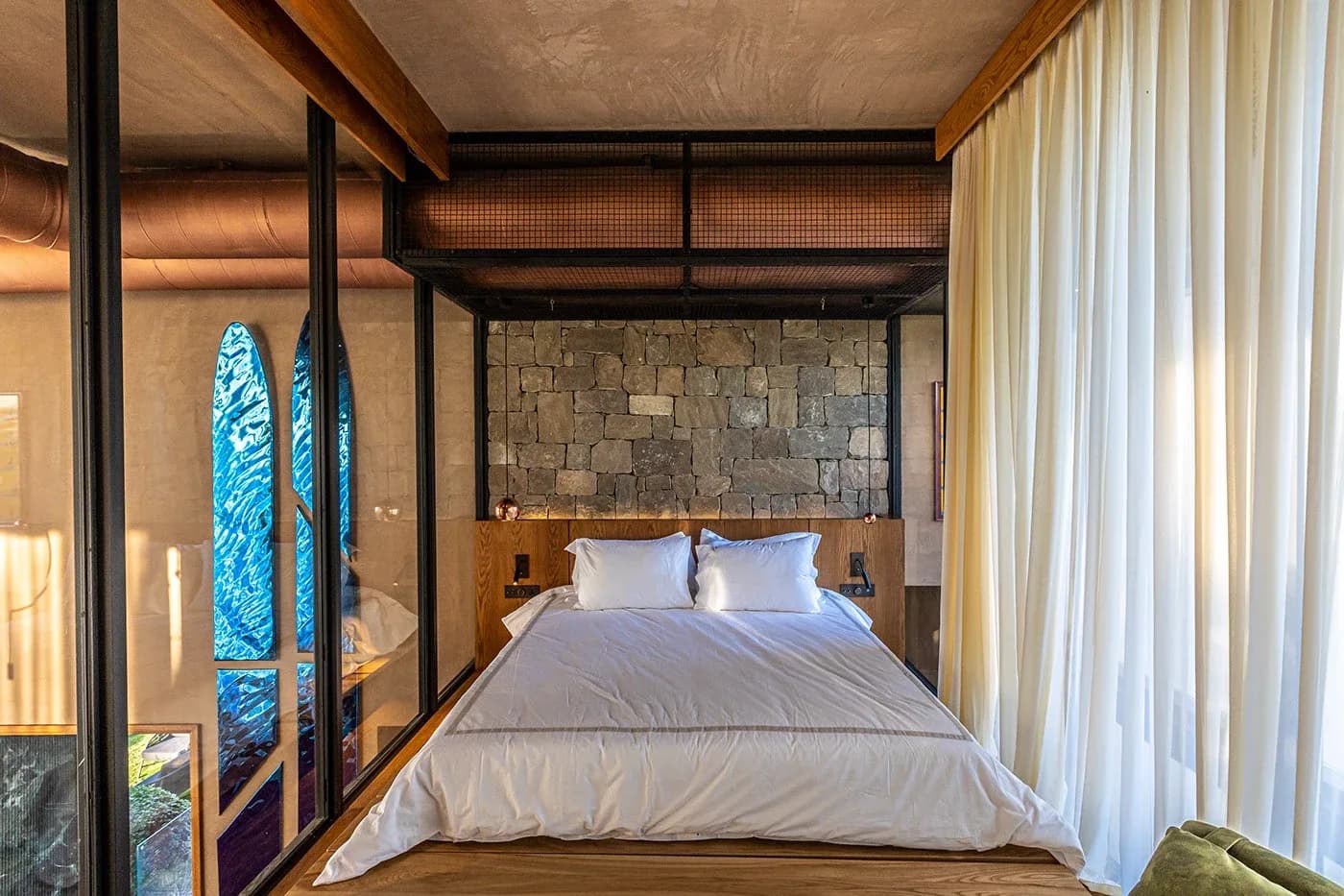 Bedroom with stone wall, white bed and sheer curtains