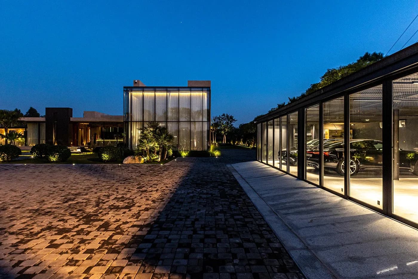 Glass garage and forecourt lit at blue hour