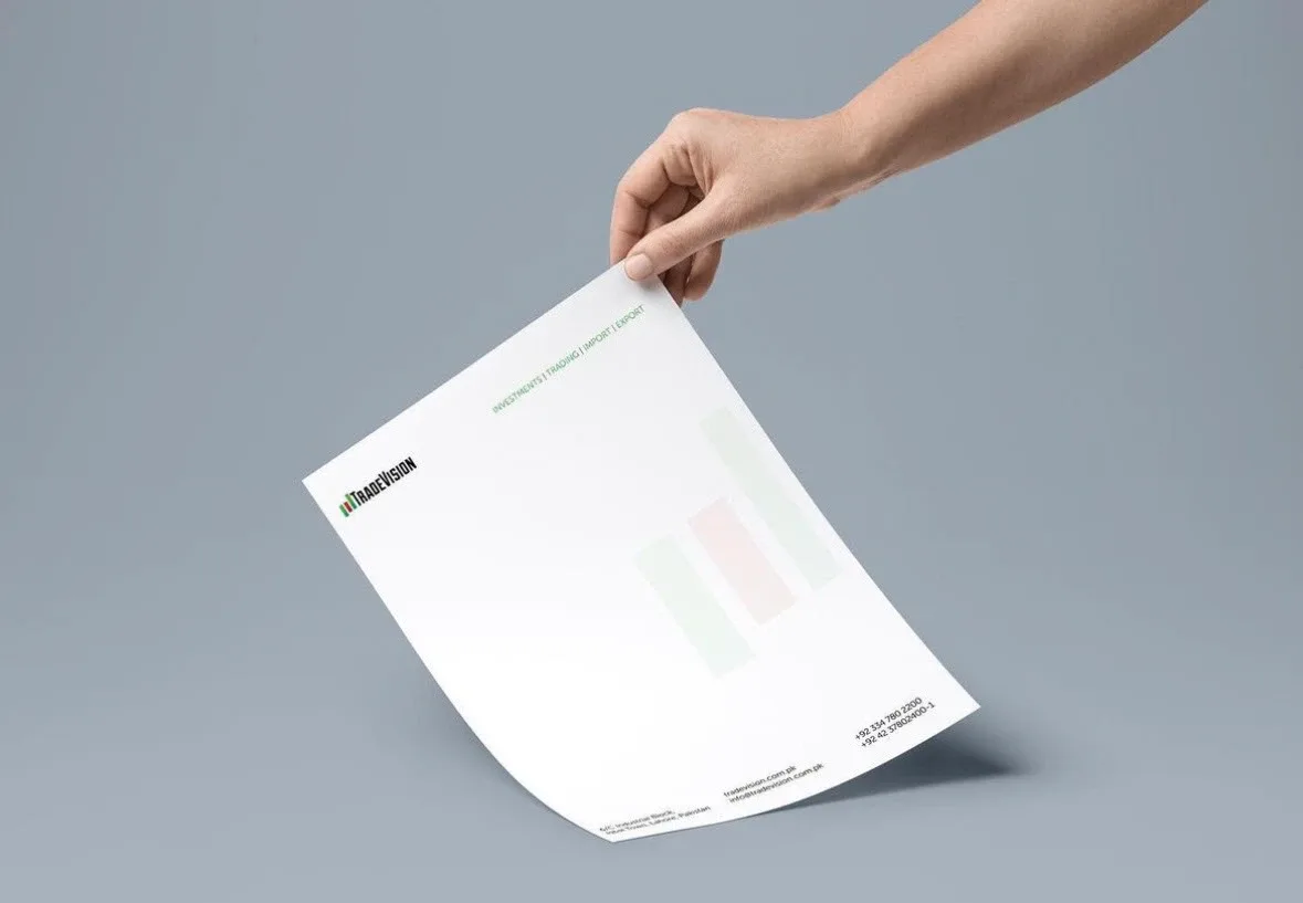 Hand holding TradeVision letterhead with faint bar-chart watermark